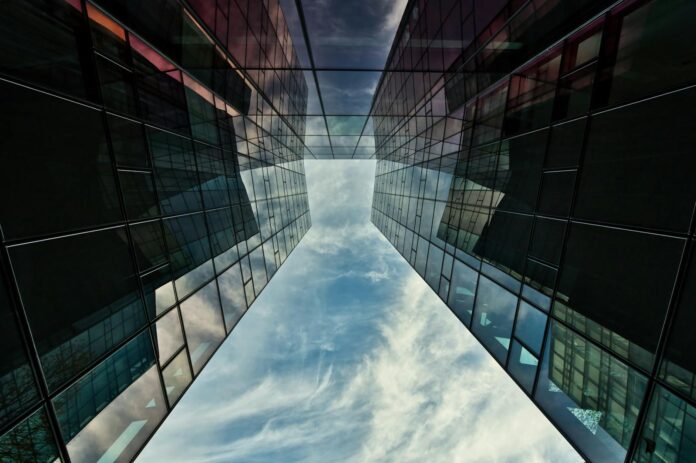 Low angle view of a modern glass facade reflecting sky in Munich, Germany.