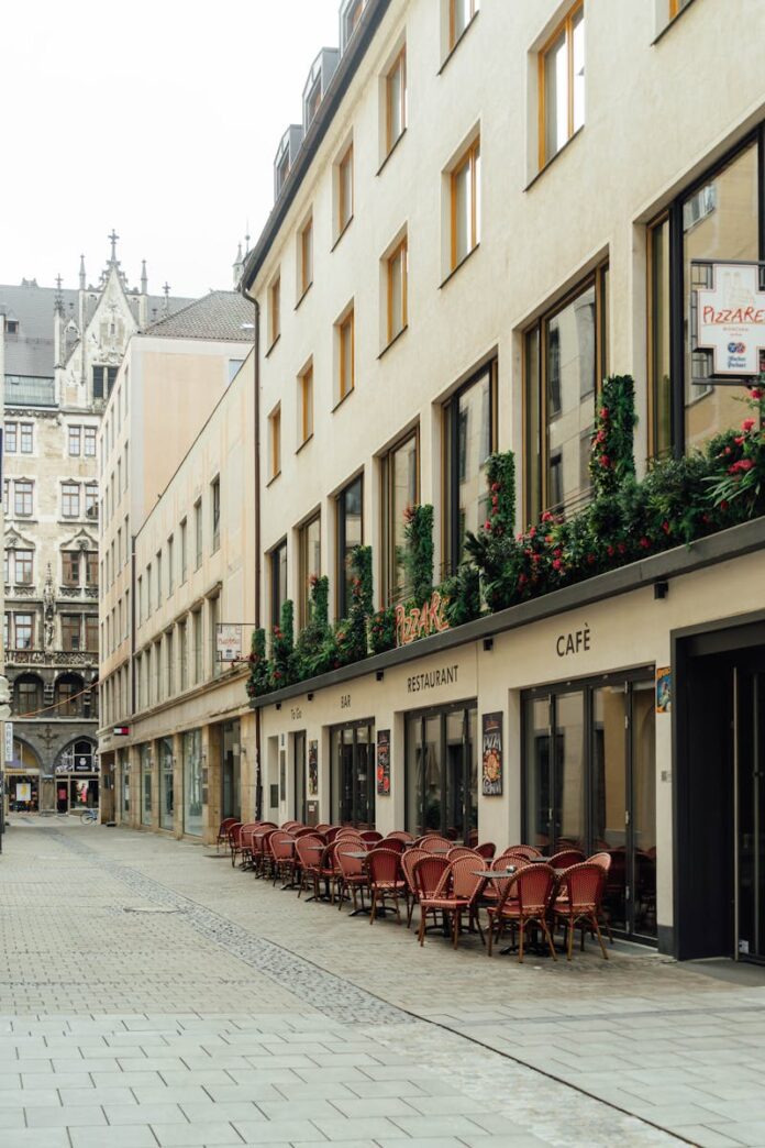 A quaint street in Munich featuring a cozy outdoor cafe with red chairs and flowers.